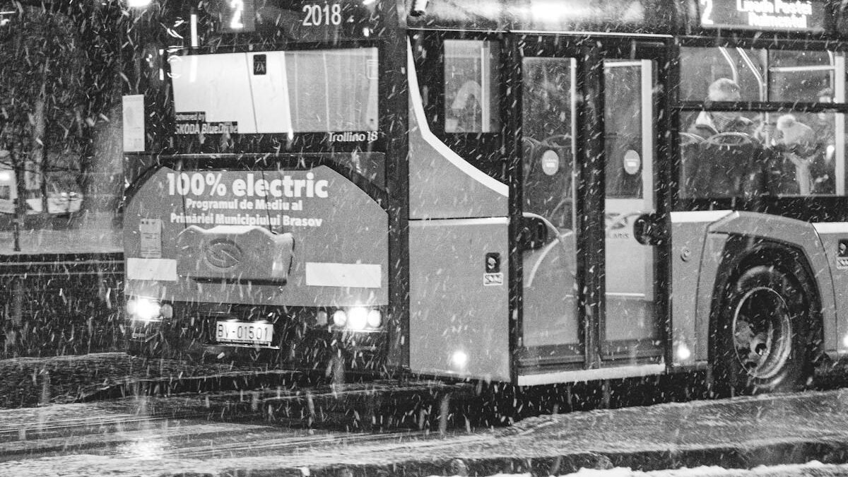Juodai balta nuotrauka su elektriniu autobusu snieguotą naktį