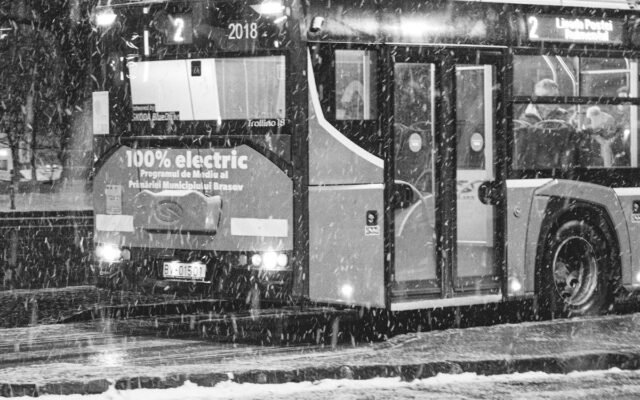Juodai balta nuotrauka su elektriniu autobusu snieguotą naktį