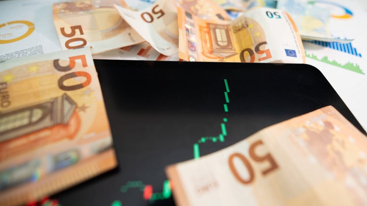 Iš arti nufotografuoti 50 eurų banknotai su skaitmenine akcijų rinkos diagrama planšetiniame kompiuteryje