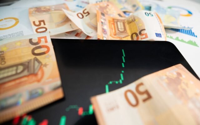 Iš arti nufotografuoti 50 eurų banknotai su skaitmenine akcijų rinkos diagrama planšetiniame kompiuteryje