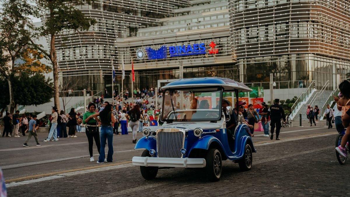 Gatvės vaizdas su elektriniu vežimėliu ir žmonėmis priešais modernų pastatą