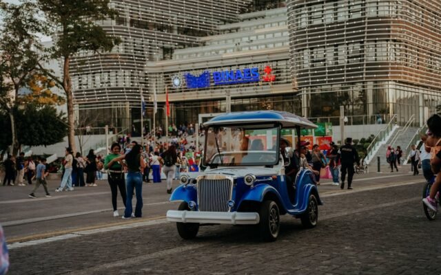 Gatvės vaizdas su elektriniu vežimėliu ir žmonėmis priešais modernų pastatą