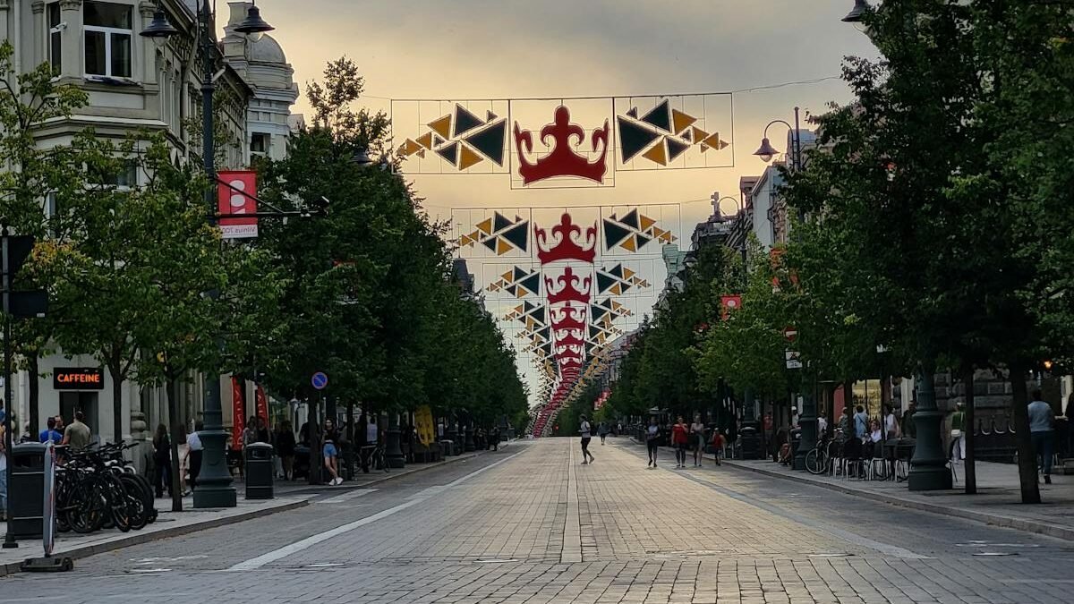 Vakarinis Gedimino prospekto vaizdas Vilniuje su virš gatvės kabančiomis dekoratyvinėmis vėliavomis