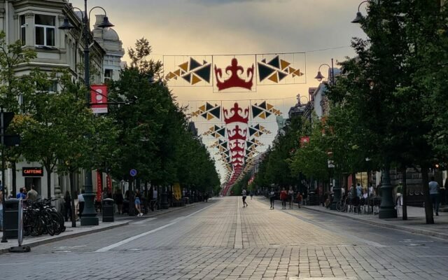 Vakarinis Gedimino prospekto vaizdas Vilniuje su virš gatvės kabančiomis dekoratyvinėmis vėliavomis