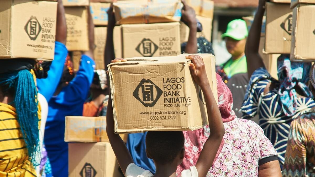 Grupė žmonių nešantys dėžes iš „Lagos Food Bank Initiative“ bendruomenės paramos renginio metu