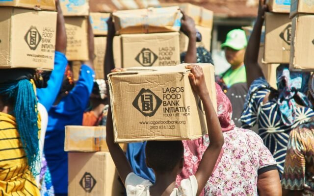 Grupė žmonių nešantys dėžes iš „Lagos Food Bank Initiative“ bendruomenės paramos renginio metu