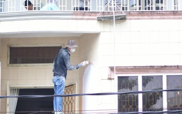 Statybininkai dažantys ir renovuojantys pastato fasadą lauke dienos metu