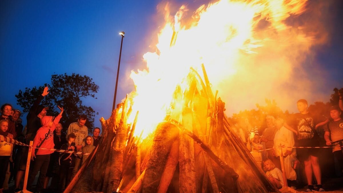 Žmonės susirinkę prie didelio laužo šventinio vakaro metu lauke